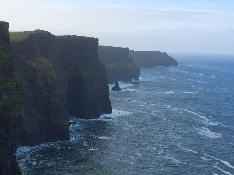 The Cliffs of Moher fading north into sea haze, O'Brien's Tower just visible on the far headland