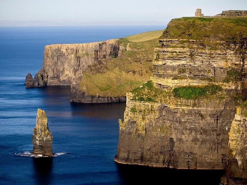 The sea stack below the Cliffs of Moher, the cliff wall rising behind it